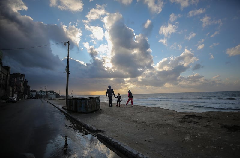 A Palestinian father and his kids walk near the beach during a cold weather at al Shatea refugee camp in Gaza City. EPA