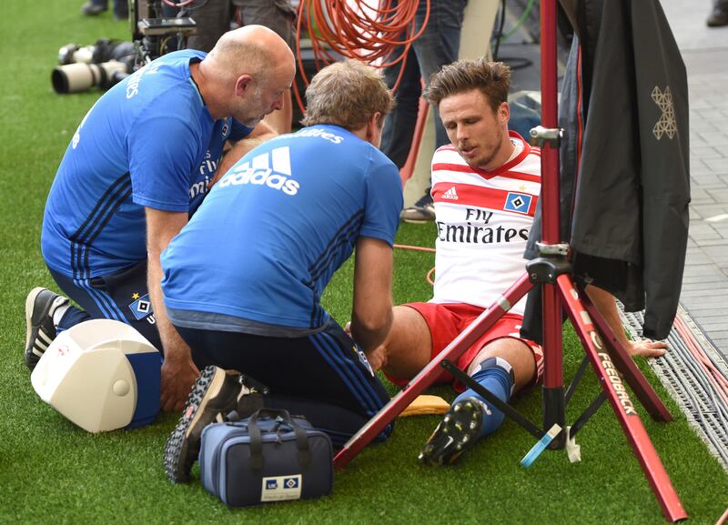 In this Aug. 19, 2017 photo Hamburg's Nicolai Mueller is treated during the German Bundesliga soccer match between Hamburger SV and  FC Augsburg in Hamburg, Germany. Hamburger SV forward Nicolai Mueller is out for around six months after injuring himself while celebrating a goal. The Bundesliga club says Mueller tore a cruciate ligament in his right knee after scoring in Saturday's league-opener, a 1-0 home win over Augsburg. Mueller attempted a pirouette before falling to the ground in apparent pain.  (Daniel Bockwoldt/dpa via AP)
