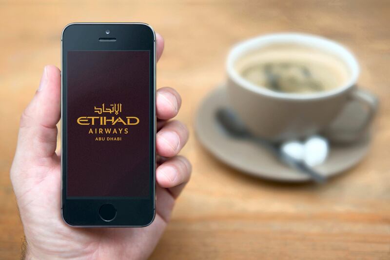 GNKFGY A man looks at his iPhone which displays the Etihad Airways logo, while sat with a cup of coffee (Editorial use only).