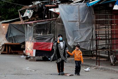 A mask-clad woman and boy walk past shuttered shops and stalls in Souk Sabra in the southern suburbs of the Lebanon's capital Beirut on January 16, 2021, despite a national total lockdown as a measure against the COVID-19 coronavirus pandemic.  / AFP / ANWAR AMRO
