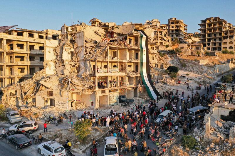 An aerial view of Syrians gathering for a demonstration by the ruins of a building that was hit in prior bombardment and adorned with a giant flag of the Syrian opposition, in the town of Ariha in the rebel-held northwestern Idlib province.  AFP