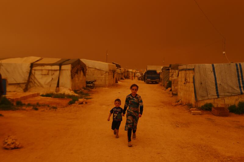 Displaced children walk past tents in Dana as dust blows. AFP