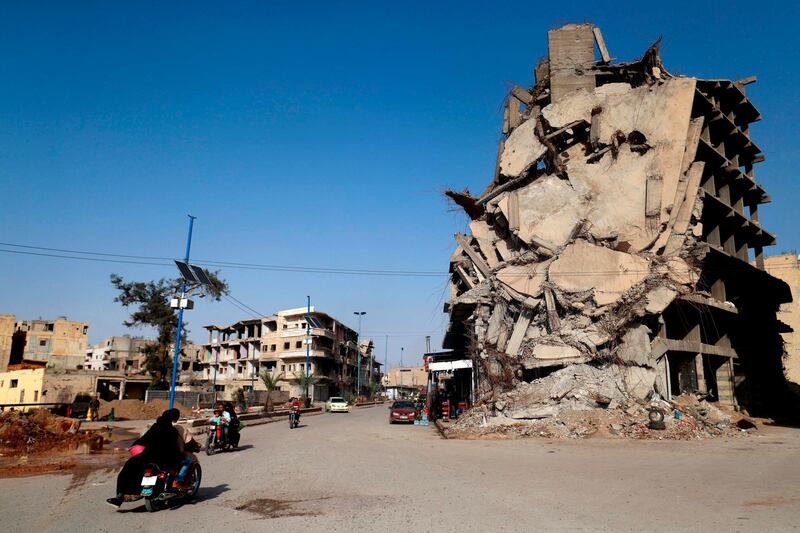 TOPSHOT - Syrians ride their motorcycles past a damaged building in the Syrian city of Raqa on October 18, 2018. A year after a US-backed alliance of Syrian fighters drove the Islamic State group from the northern city of Raqa, traumatised civilians still live in fear of near-daily bombings. / AFP / Delil souleiman
