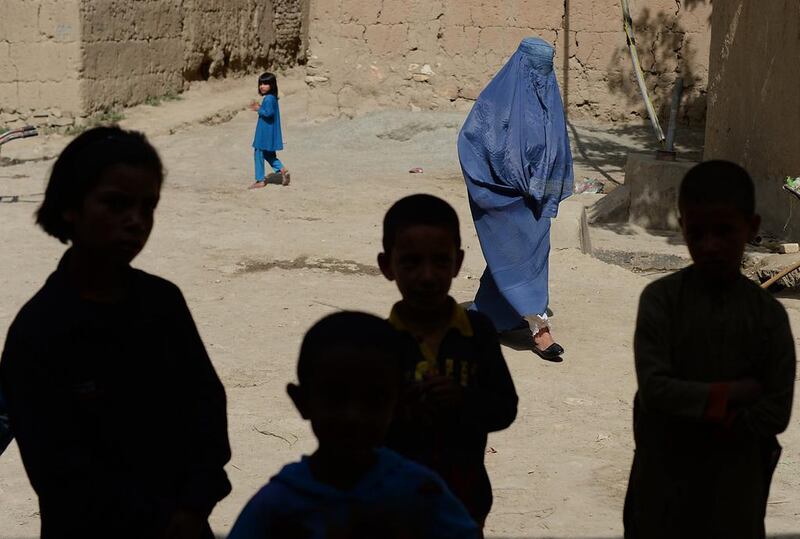 A burqa-clad Afghan villager walks past children as they stand in the shadows of buildings in the village of Laghmani on The Shomali Plains some 20 kms north of Kabul. Shah Marai / AFP 