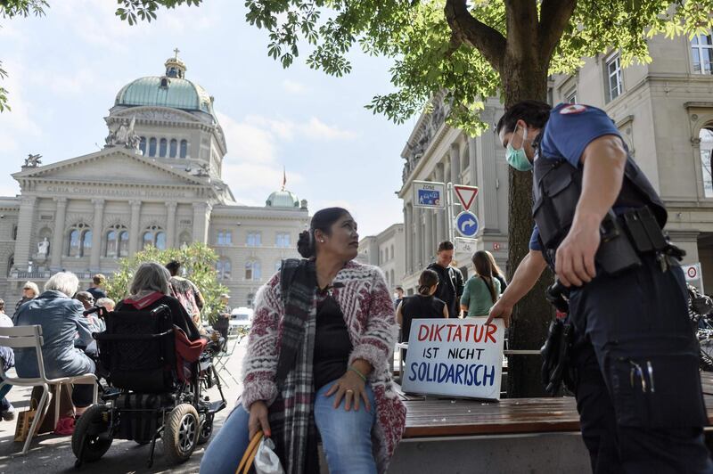 A police officer wearing a protective face mask removes a placard reading in German: "Dictature is not solidarity" at an anti-coronavirus lockdown demonstration in Bern on May 16, 2020, following an easing of lockdown measures in Switzerland during the Covid-19 pandemic.   AFP