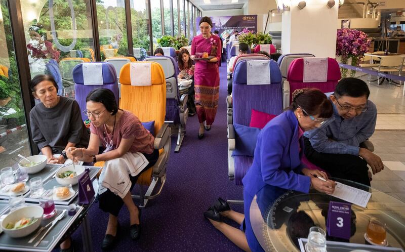 A flight attendant serves welcome drinks in a flight-themed restaurant at the Thai Airways head office in Bangkok, Thailand on Oct. 3, 2020. The airline is selling time on its flight simulators to wannabe pilots while its catering division is serving meals in a flight-themed restaurant complete with airline seats and attentive cabin crew. The airline is trying to boost staff morale, polish its image and bring in a few pennies, even as it juggles preparing to resume international flights while devising a business reorganization plan.  (AP Photo/Sakchai Lalit)