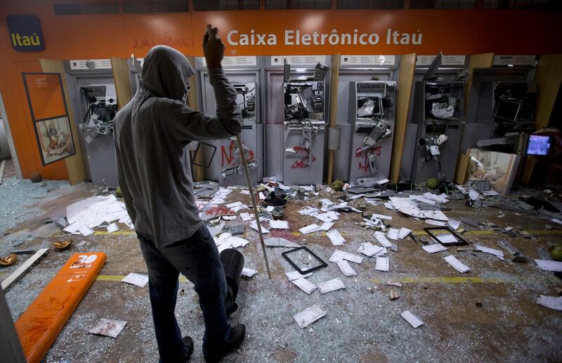 A protester looks at vandalized cash machines at a bank during a demonstration in Rio de Janeiro, Brazil, Monday, June 17, 2013. Thousands took to the streets in largely peaceful protests in at least eight cities in Brazil Monday, demonstrations that voiced the deep frustrations Brazilians feel about carrying heavy tax burdens but receiving woeful returns in public education, health, security and transportation. Officers in Rio fired tear gas and rubber bullets when a group of protesters invaded the state legislative assembly and later vandalized and looted properties in the area.(AP Photo/Victor R. Caivano) *** Local Caption ***  Brazil Confed Cup Protest.JPEG-00c5e.jpg