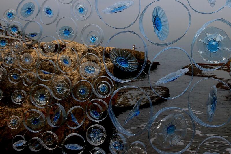 A fisherman tries his luck in the Mediterranean Sea as pieces of plastic bottles collected by activists hang on a wall, next to a rocky coastal area in Beirut, Lebanon. AP