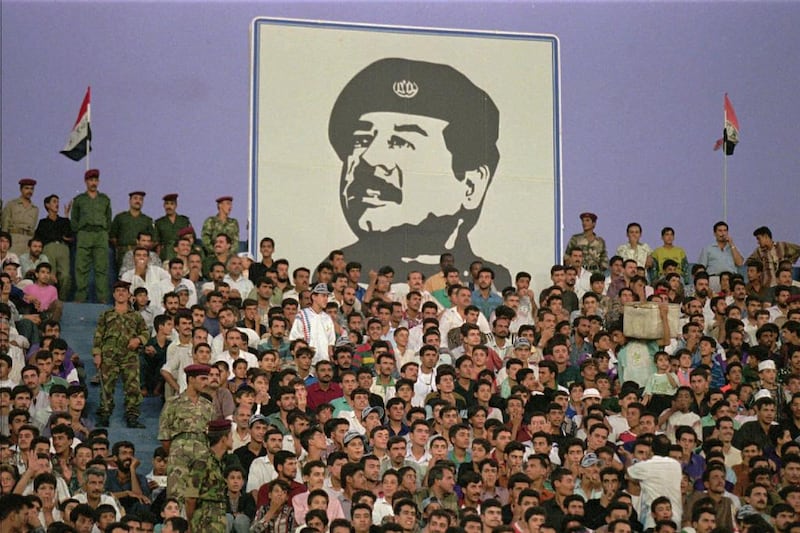 Football fans sit under a portrait of Saddam Hussein at Al Sha'ab Stadium in Baghdad in 1996. Faisal Al Yafai imagines a world where Saddam maintained control over Kuwait. (John Moore / AP Photo)
