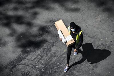 A delivery man wearing a protective mask carries an Amazon box and a letter in a street of Paris on April 15, 2020 on the 30th day of a lockdown in France aimed at curbing the spread of the COVID-19 infection caused by the novel coronavirus. (Photo by JOEL SAGET / AFP)