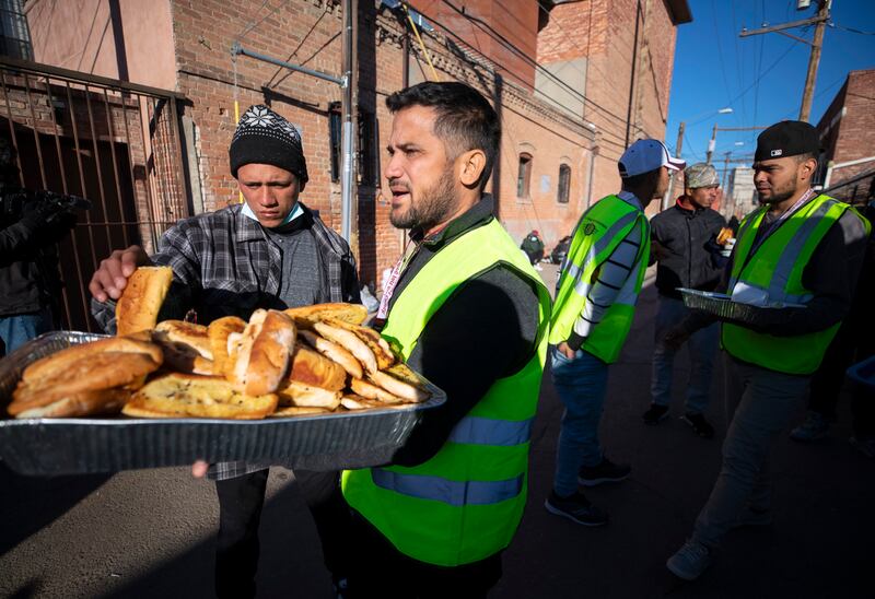 Church volunteers serve garlic bread to migrants camping outside. AP