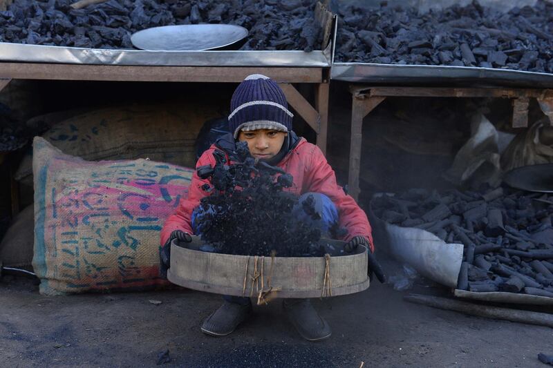 A young Afghan vendor sifts charcoal at his stall in Herat city. AFP