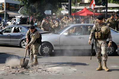 A soldier removes remains of burnt tires placed by anti-government protesters to block a road, as others stand guard in Hazmiyeh, a suburb of Beirut, Lebanon, Tuesday, Nov. 5, 2019. Lebanese troops are deploying in different parts of the country forcefully opening roads closed by anti-government protesters. (AP Photo/Bilal Hussein)