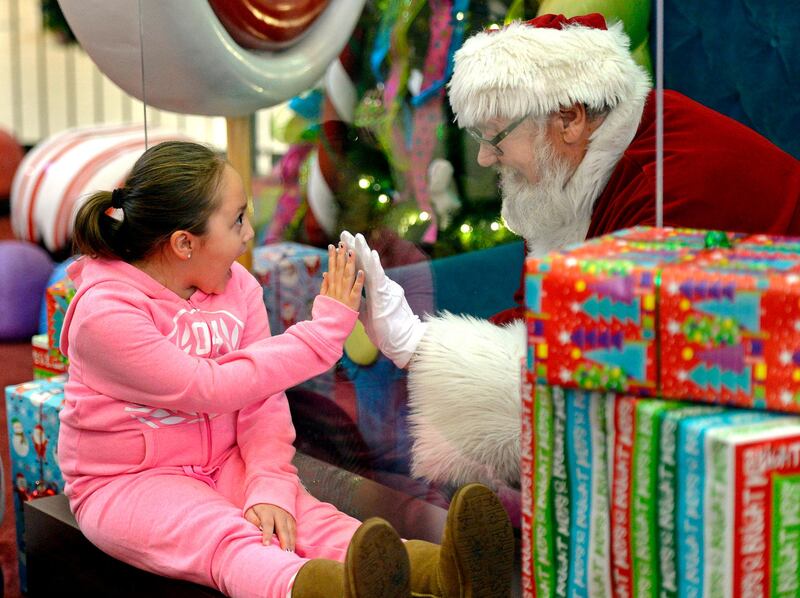 Madalynn Brooks, 7, of Canadohta Lake, visits with Santa Claus at the Millcreek Mall, in Millcreek Township, Pennsylvania. Santa, portrayed by Lenny Chatt, 73, of Lawrence Park, was seated behind a sheet of plexiglass due to Covid-19 safety measures.  AP