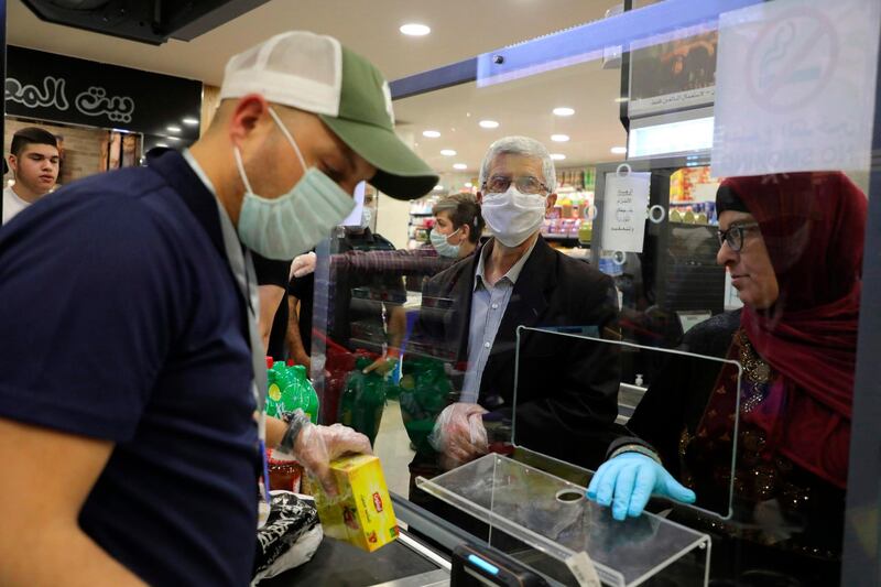 Palestinians, wearing protective masks due to the COVID-19 coronavirus pandemic, pay for their shopping at the checkout counter of a supermarket on the last day before the start of the Muslim holy month of Ramadan, beginning later in the night, at a supermarket in the city of Hebron in the occupied West Bank on April 23, 2020.  / AFP / HAZEM BADER

