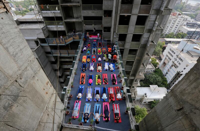 Indians performs yoga on a walk-way between two towers of an under construction high rise residential building as they mark International Yoga Day in Ahmadabad, India. Ajit Solanki / AP Photo