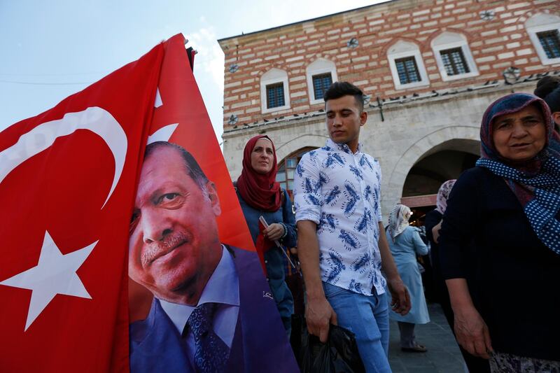 People walk past a street vendor offering Turkish flags for sale, at a market in Istanbul, Thursday, Aug. 16, 2018.Turkey's finance chief tried to reassure thousands of international investors on a conference call Thursday, in which he pledged to fix the economic troubles that have seen the country spiral into a currency crisis.The national currency recovered somewhat from record lows hit earlier this week. (AP Photo/Lefteris Pitarakis)