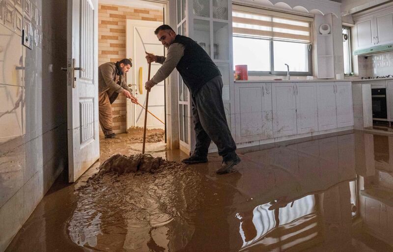 People clear water from their flooded homes in Arbil, the capital of Iraq's northern Kurdish autonomous region, in the aftermath of flash floods following heavy rain on January 13, 2022.  (Photo by SAFIN HAMED  /  AFP)