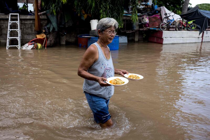 A woman carries plates of food through floodwaters in a neighbourhood in Ayutthaya, Thailand on October 4, after a tropical storm flooded 31 provinces across the country. AFP