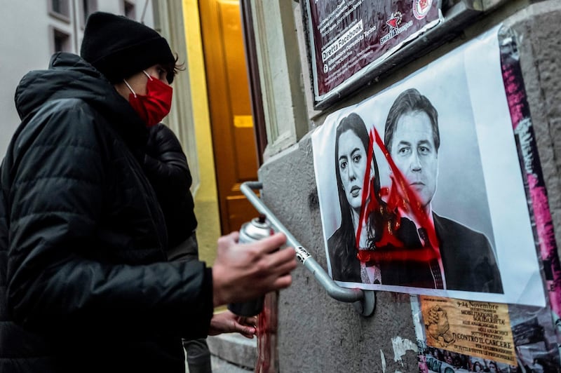 A student paints graffiti on pictures of Minister of Education Lucia Azzolina and Italian Prime Minister Giuseppe Conte pasted on a wall at the entrance of a school in Turin. AFP