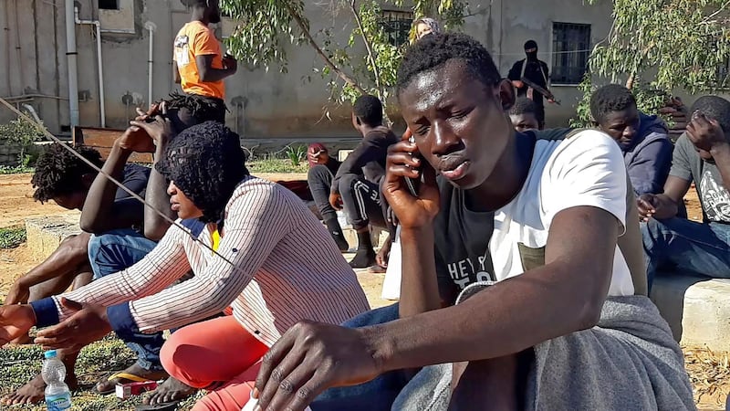 A migrant, who survived a deadly shipwreck, speaks on the phone as he gathers with other survivors on a sandy beach on the coast of al-Khums, a port city 120 kilometres (75 miles) west of the Libyan capital Tripoli, on November 12, 2020. A shipwreck off the Libyan coast has killed 20 people, Doctors Without Borders (MSF) said, just hours after news of a separate incident in which at least 74 migrants died. / AFP / -
