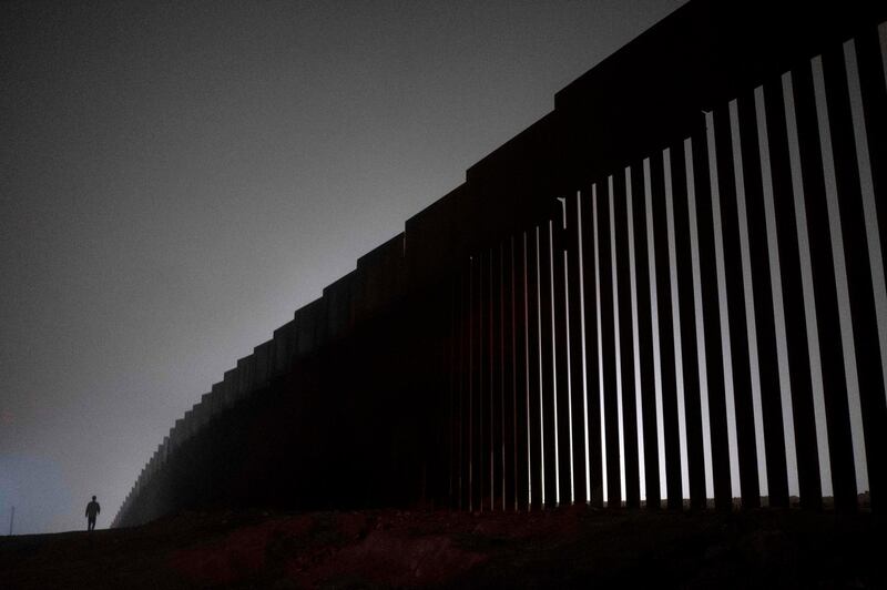 TOPSHOT - A man walks next to a reinforced section of the US-Mexico border fence is seen from Tijuana, Baja California state, Mexico on December 20, 2018.  Donald Trump and congressional Democrats stood at stark odds on December 20, 2018, as the president balked at a spending stopgap that contains no border wall funding, leaving the US government on the precipice of a Christmastime shutdown. / AFP / Guillermo Arias
