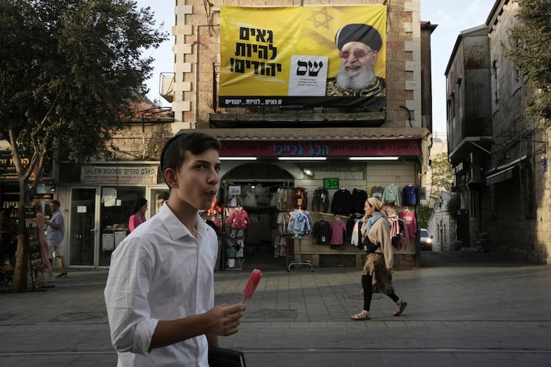 A popsicle break beneath an election campaign hoarding for Israel's ultra-Orthodox Shas political party near Mahane Yehuda market in Jerusalem. Israelis are back at the polls for a fifth time in less than four years. AP