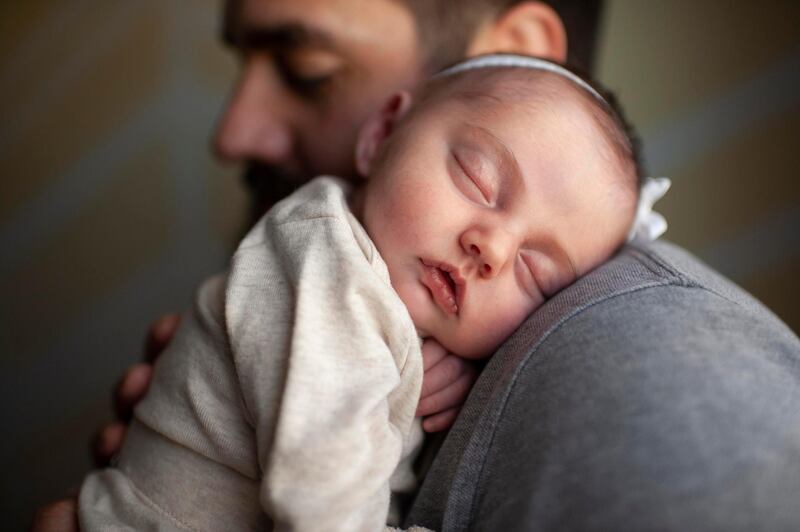 Close up of newborn baby's face sleeping on father's shoulder at home. Getty Images