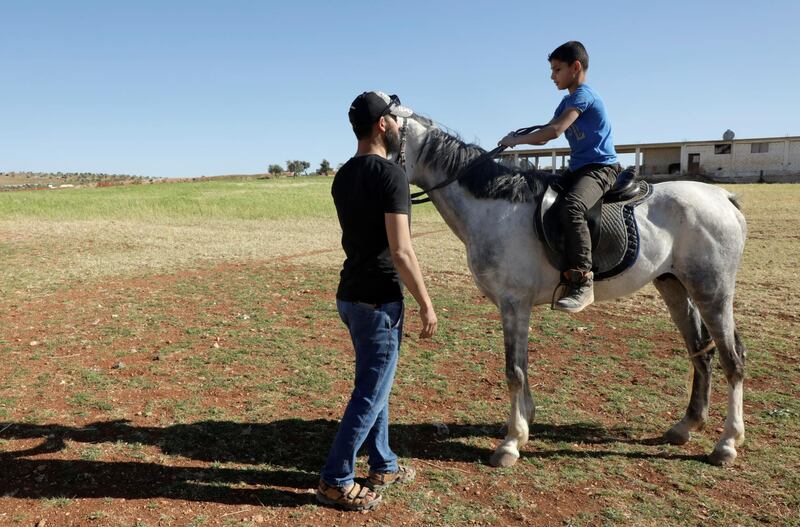 Abu Ibrahim al-Zaim, owner of Zaim farm, teaches a boy to ride in Idlib, Syria. Reuters