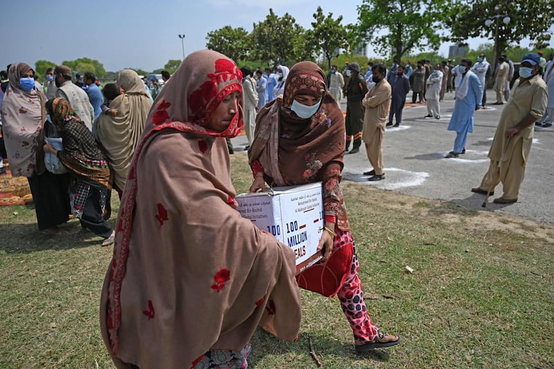 Women in need carry foodstuff being distributed by the UAE embassy in Islamabad.