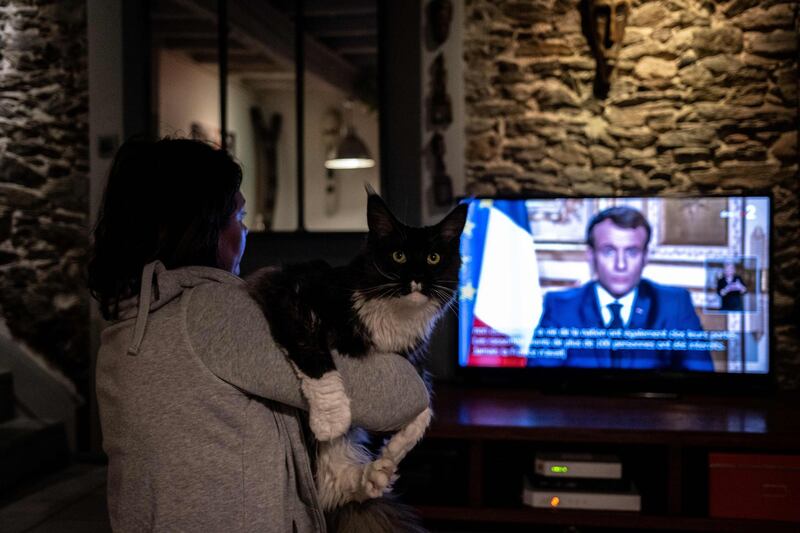 A person in Givord, near Lyon, holds a cat while watching French President Emmanuel Macron give a televised address to the nation on the outbreak of coronavirus, on March 16, 2020.  AFP