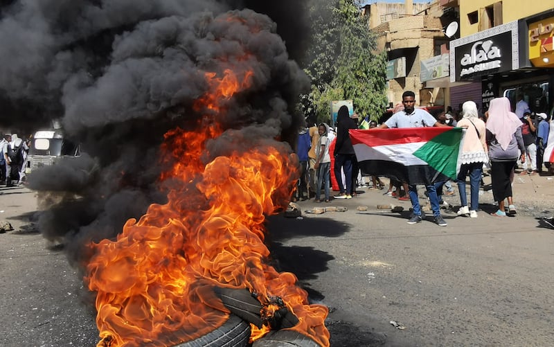 Sudanese protesters walk past burning tyres during a rally. AFP