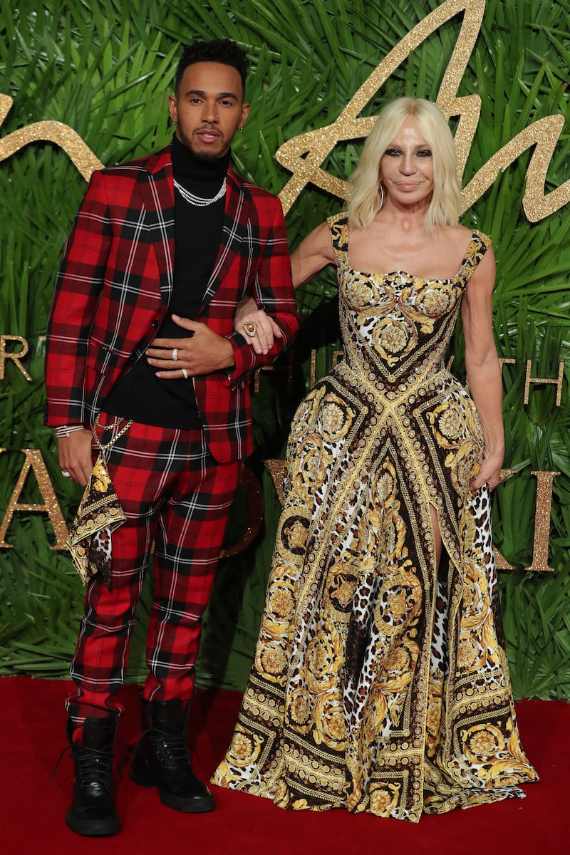 Lewis Hamilton, in a red tartan suit and black turtleneck jumper by Versace, and Donatella Versace arrive at the British Fashion Awards in London on December 4, 2017. AFP