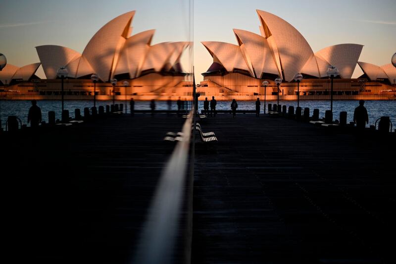 TOPSHOT - Sunset hues fall on the landmark Sydney Opera House as it is seen in a reflection from Circular Quay, usually packed with tourists, in Sydney on June 16, 2020. / AFP / Saeed KHAN

