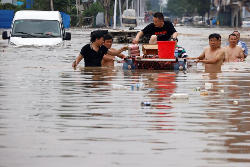 People with a makeshift raft look for others to rescue in Zhengzhou, where the floodwater is chest-high in some areas.
