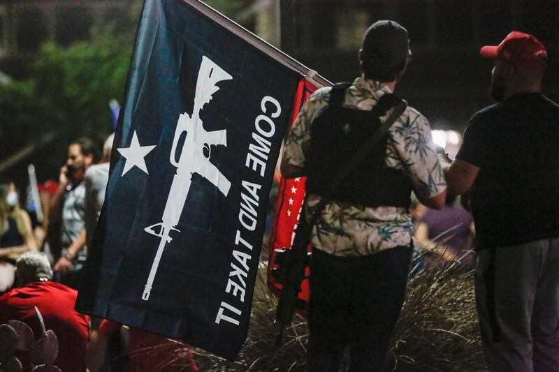 A member of the Boogaloo Boys movement holds a flag while attending a protest about the early results of the 2020 presidential election, in front of the Maricopa County Tabulation and Election Centre in Phoenix, Arizona. Reuters