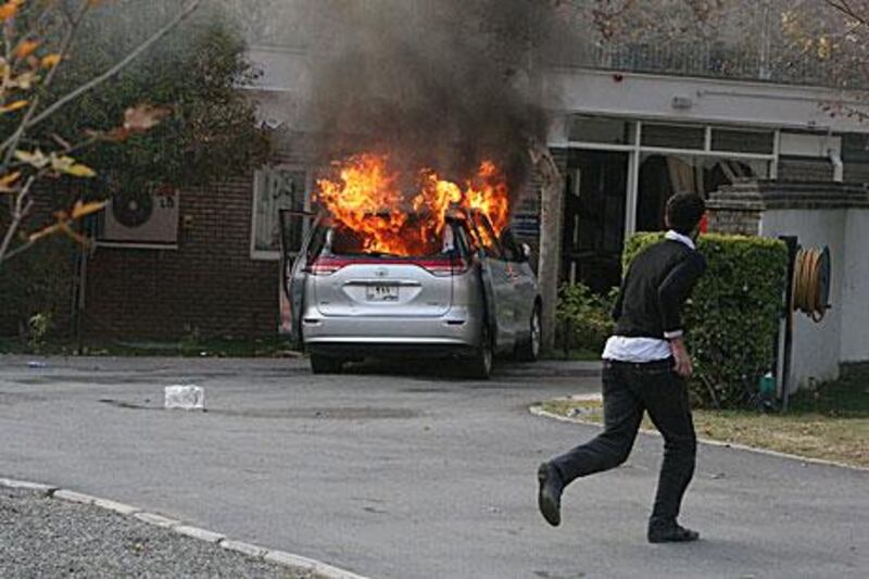 An Iranian protester runs inside the British embassy in Tehran as a diplomatic vehicle is ablaze during Tuesday's storming of British compounds in the country.