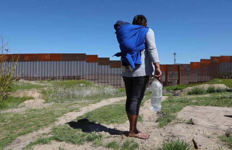 A migrant carrying a toddler stands in front of the border wall that divides Sunland Park, New Mexico, United States, with Ciudad Juarez, state of Chihuahua, Mexico on March 14, 2020. April 22, 2020 commemorates the 50th anniversary of the World Earth Day. / AFP / HERIKA MARTINEZ
