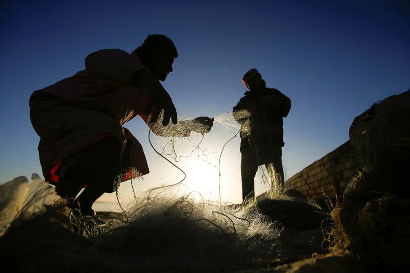Fishermen are silhouetted against the low sun as they sort their fishing nets by the Najaf Sea. The lake formed in a tectonic depression expanded by weathering. Reuters