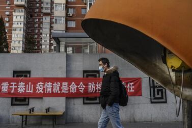 A Chinese man wears a protective mask as he walks by a banner related to the coronavirus outbreak on a residential building in Beijing. Getty Image