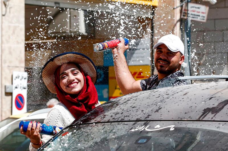 Palestinian high school students spray artificial snow from canisters while seated through the window of a moving vehicle as they celebrate the announcement of their general secondary education examination (Tawjihee) results in a car procession.  AFP