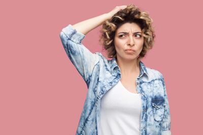 TWAK8E Portrait of thoughtful confused young woman with curly hairstyle in casual blue shirt standing scratching her head and thinking what to do. indoor stu