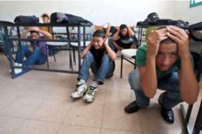 Palestinian schoolboys take cover under their desks in a classroom at a public school in the east Jerusalem neighbourhood of Issawiya as Israel held its largest-ever emergency drill on May 26, 2010. Air raid sirens wailed across Israel at the peak of a five-day civil defence exercise to test the Jewish state's defences in the event of war, the army said. Radio stations broadcast a pre-recorded message saying the siren was part of a drill but asking people to go down to the shelters. TOPSHOTS/AFP PHOTO/AHMAD GHARABLI *** Local Caption ***  617234-01-08.jpg