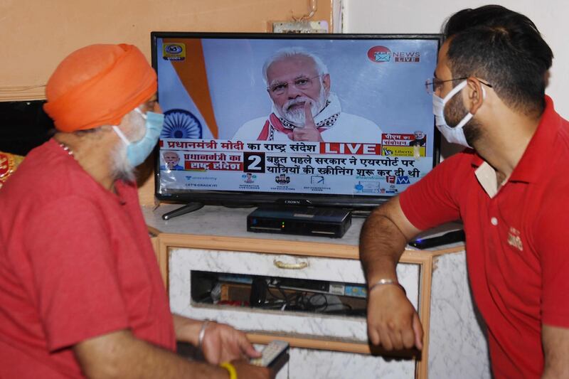 Residents wearing face masks watch Mr Modi's address to the nation r.  AFP