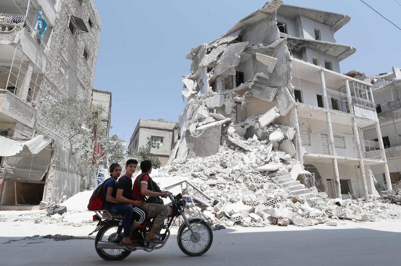 A Syrian man drives a motorcycle past destroyed buildings in the town of Ariha, in the south of Syria's Idlib province, on August 2, 2019. Air strikes stopped in Syria's Idlib on August 2 after the government announced it had agreed a truce following weeks of deadly bombardment of the rebel-held region, monitors said. / AFP / Omar HAJ KADOUR
