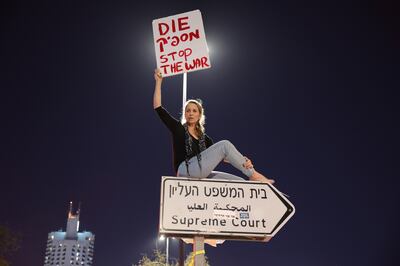 An anti-government protester sits on a street sign for the Supreme Court with a sign that reads 'Enough' in Hebrew, and 'Stop the war' in English, during a rally in Jerusalem. EPA