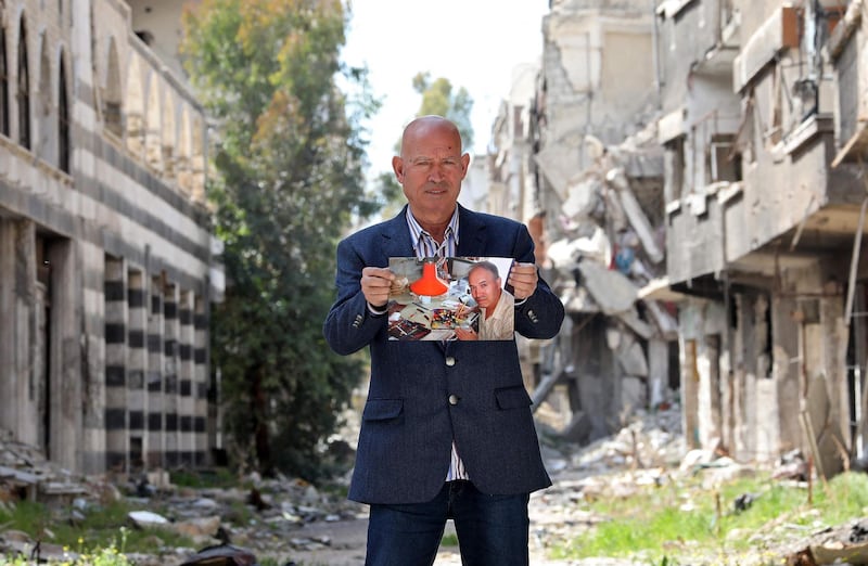 Mohammed Al Rakouia, 70, a Palestinian refugee painter from the ravaged Yarmouk camp for Palestinian refugees south of Syria's capital Damascus, stands along an alley by damaged buildings in the camp on March 7, 2021, while holding a picture of himself working in his former studio dating from ten years prior. Al Rakouia laments his losses saying "nothing can make up" for them. "My studio has been destroyed, my paintings have been stolen, and my colours have been scattered all over the place." AFP