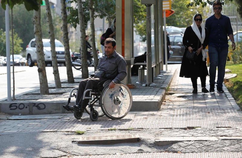 Behnam Soleimani, a 34-year-old Iranian computer teacher who uses a wheelchair, makes his way down an uneven sidewalk in Tehran on July 17, 2017.
Official figures say there are 94,000 disabled people in Tehran, though advocates say the real figure could be far higher. Few are ever seen on its busy streets, nor on the city's bus and metro system because reaching the stations is nigh-on impossible. / AFP PHOTO / ATTA KENARE
