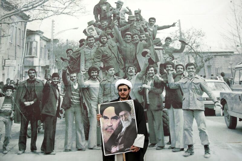 An Iranian cleric holds a poster of Ayatollah Ali Khamenei and Ayatollah Khomeini in front of a photo mural of the 1979 Islamic Revolution. Ebrahim Noroozi / AP Photo