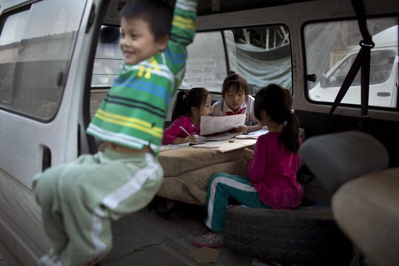 Chinese girls do their homework inside a delivery van while a boy enjoys swinging from the van's door at a second-hand furniture market in Beijing, China. Alexander F Yuan / AP Photo